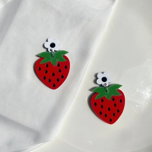 Close-up of cute acrylic strawberry earrings with small white flower on a white ceramic tray