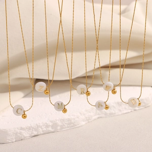 18K gold plated stainless steel necklaces with white letter pendants on beige fabric