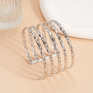 Detail of silver layered wave cuff bracelet on a warm beige background with luxury texture