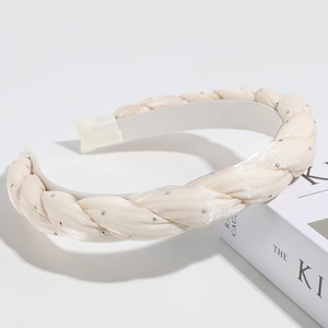 Close-up of ivory braided satin headband with sparkling rhinestones on white surface