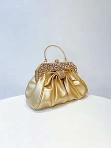 Detail of gold evening clutch bag with rhinestone and pearl handle on pleated fabric
