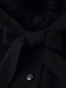 Détail d'un manteau d'hiver noir montrant un grand nœud et un col en fausse fourrure douce