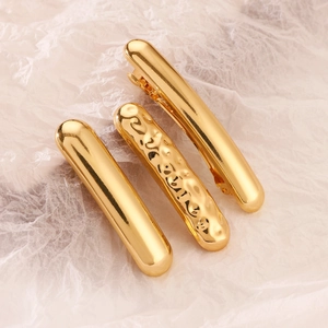 Close-up of three gold alloy geometric hair clips with smooth and hammered metal textures