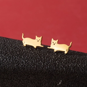 Close-up of golden cartoon cat stud earrings on a textured black leather surface