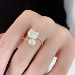 Macro detail of golden open ring featuring a white cat shell motif and round pearl