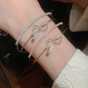 Close-up of layered zircon bow bracelets in gold and silver finish on a female wrist