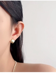 Detailed close-up of a minimalist gold square stud earring worn by a female model
