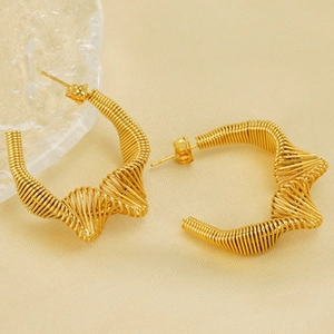 Detail of gold twisted wire hoop earrings with metallic texture on beige background