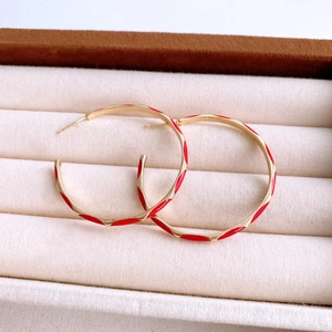 Close-up of golden hoop earrings with red enamel coating and bamboo textured finish