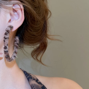 Detail of plush leopard print hoop earring on model with vintage brown fur texture