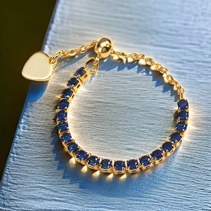 Detail of adjustable gold ring with blue round zircons and delicate heart pendant
