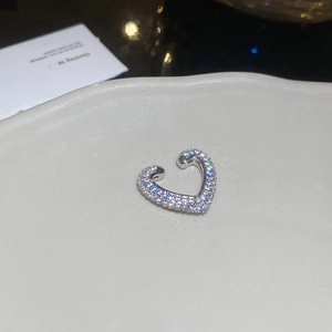 Macro shot of silver heart-shaped ear cuff with sparkling cubic zirconia on ceramic tray