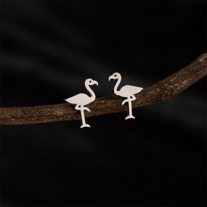 Minimalist silver flamingo stud earrings displayed on natural wood branch over black background