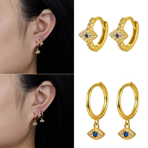 Detailed close-up of golden evil eye hoop earrings with blue stones and zircon inlay