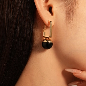 Close-up of golden geometric rectangle earrings with black round resin bead on female model