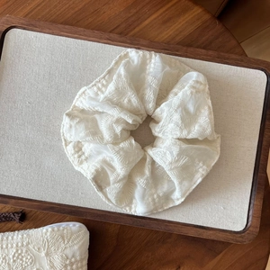 Close-up of a white lace embroidered oversized scrunchie on a wooden tray detail
