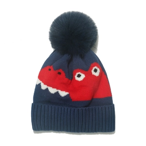 Winter knit baby beanie featuring cartoon dinosaur patterns and a plush blue faux fur pom