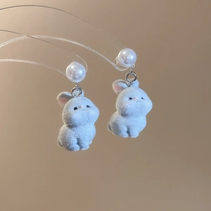 Close-up of light blue flocked rabbit earrings with white pearl studs on a clear stand