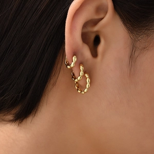 Close-up of three gold twisted hoop earrings worn on ear showing layered texture