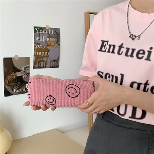 Pink corduroy makeup pouch with embroidered smiley face shown held by a person
