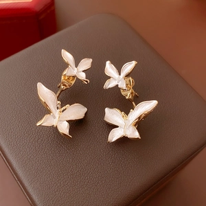 Gros plan sur les boucles d'oreilles papillon dorées en émail blanc sur cuir brun
