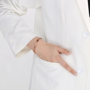 Detail of a rose gold Cuban link bracelet on a wrist with a white professional suit