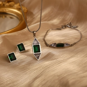 Parure en argent avec pierres vert émeraude sur fond luxueux de soie dorée et miroir rétro