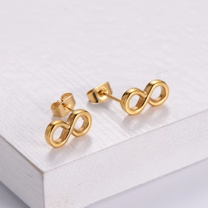 Boucles d'oreilles minimalistes symbole infini en or poli sur une surface bois blanc