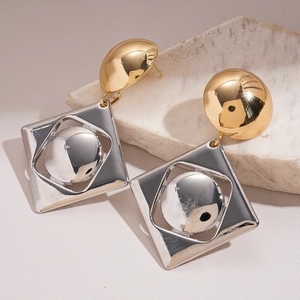 Detail of geometric mixed gold and silver metal earrings on a marble stone surface
