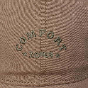 Macro shot of green 'COMFORT ZONES' embroidery on a khaki cotton twill baseball cap