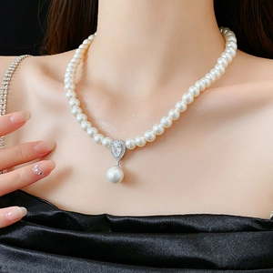 Detail of white pearl necklace with zircon teardrop pendant on female neck and collarbone