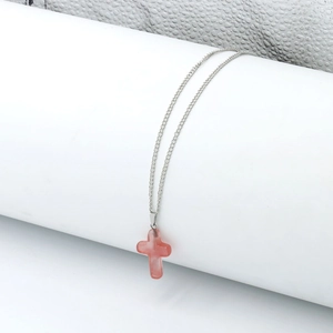 Detail view of pink crystal cross pendant on a silver metal chain hanging on a white prop