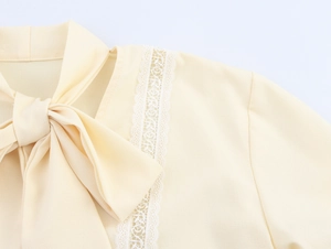 Detail of lace trim and bow tie neckline on an elegant light yellow lantern sleeve blouse
