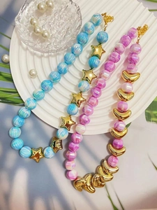 Dettaglio di collane di perle stile Hawaii con ciondoli dorati a forma di stella e luna.