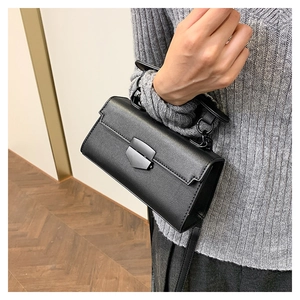 Detail of black cross-grain leather handbag featuring a round metal handle and shield lock