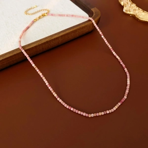 Vue à plat d'un collier bohème en perles roses avec pierres naturelles carrées sur bois