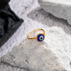 Detailed macro view of handmade gold wire wrapped ring with blue evil eye bead on a rock