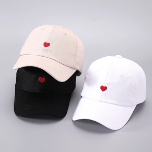 Close-up of heart embroidery detail on stacked beige, black and white cotton baseball caps