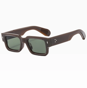 Détail de lunettes de soleil carrées marron translucide avec verres verts et rivets