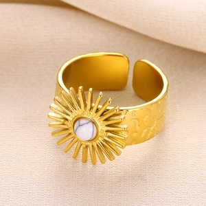 Detail of vintage sunburst gold ring with central white marble stone on beige fabric