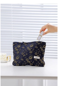 Detail of hand placing lipstick into a navy blue floral embroidered canvas cosmetic bag