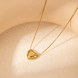 Dettaglio del ciondolo a cuore dorato con zirconi brillanti incastonati su una catena sottile