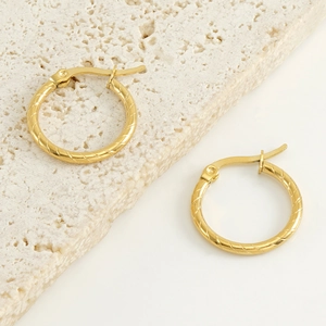 Textured gold circle hoop earrings with clicker closure on minimalist beige stone base