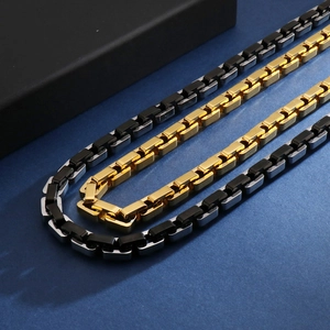Makroaufnahme geometrischer Vierkantketten aus Gold, Silber und schwarzem Edelstahl