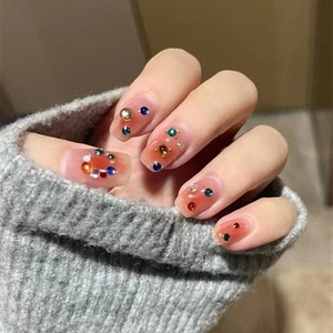 Close-up of pink gradient press-on nails with colorful rhinestones and metal beads