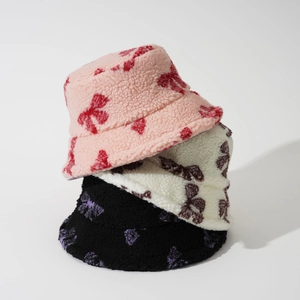 Three bow-patterned plush bucket hats in pink, white, and black with soft fleece texture