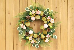 Detail of Christmas wreath with pink roses, pine cones, and green leaves on wood