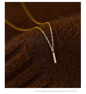 Close-up of golden vertical bar pendant with micro-set zircon on brown fabric