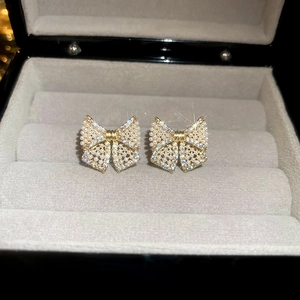 Elegant gold bow earrings with micro-inlaid pearls and rhinestones on a velvet base