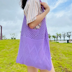 Purple hollow knit tote bag worn by a model on a shoulder in a sunny outdoor setting